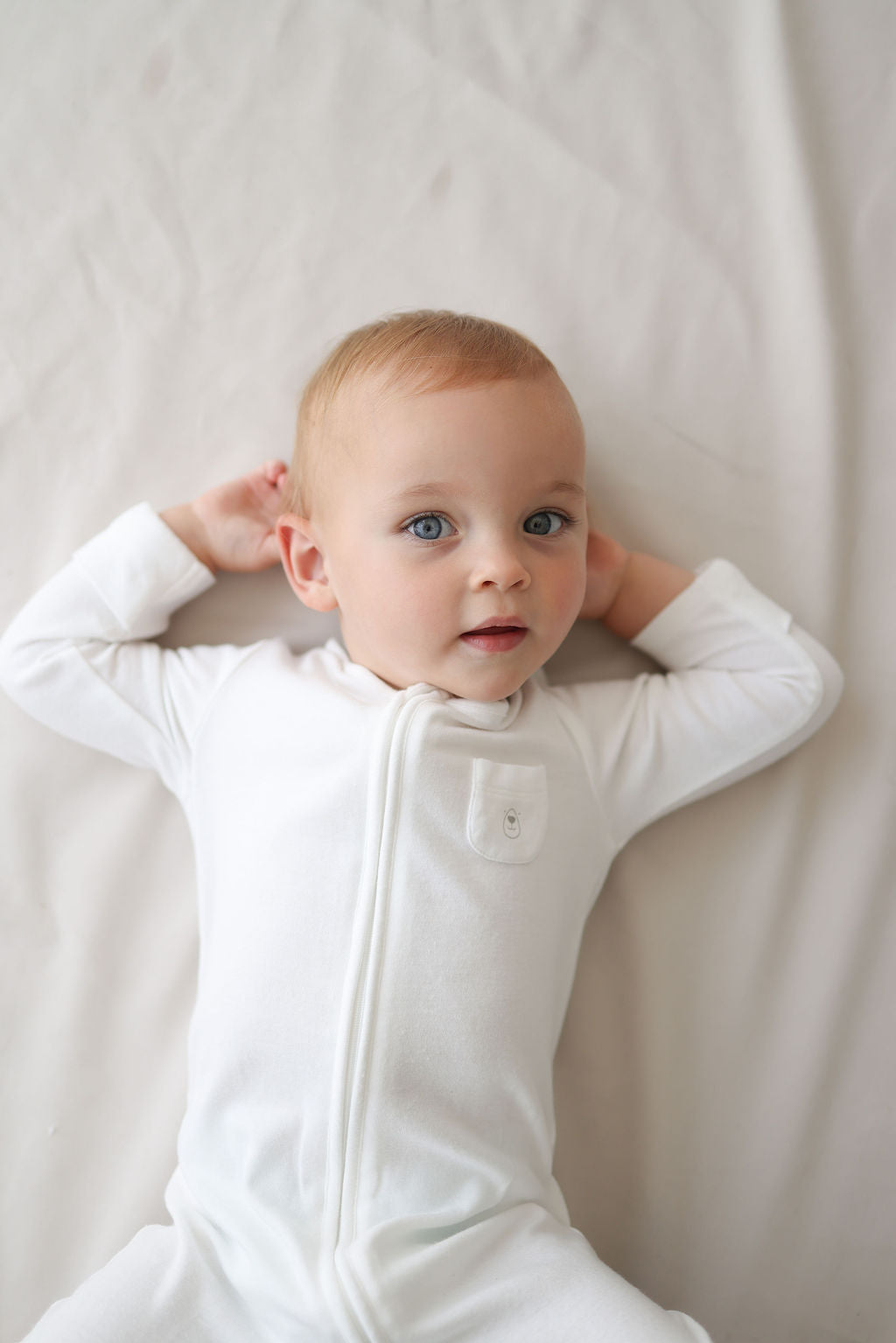 Baby wearing a white onesie against a plain background