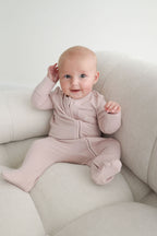Baby in a pink outfit sitting on a light-colored couch.