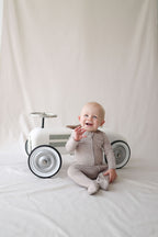 Baby sitting next to a white toy car on a plain background