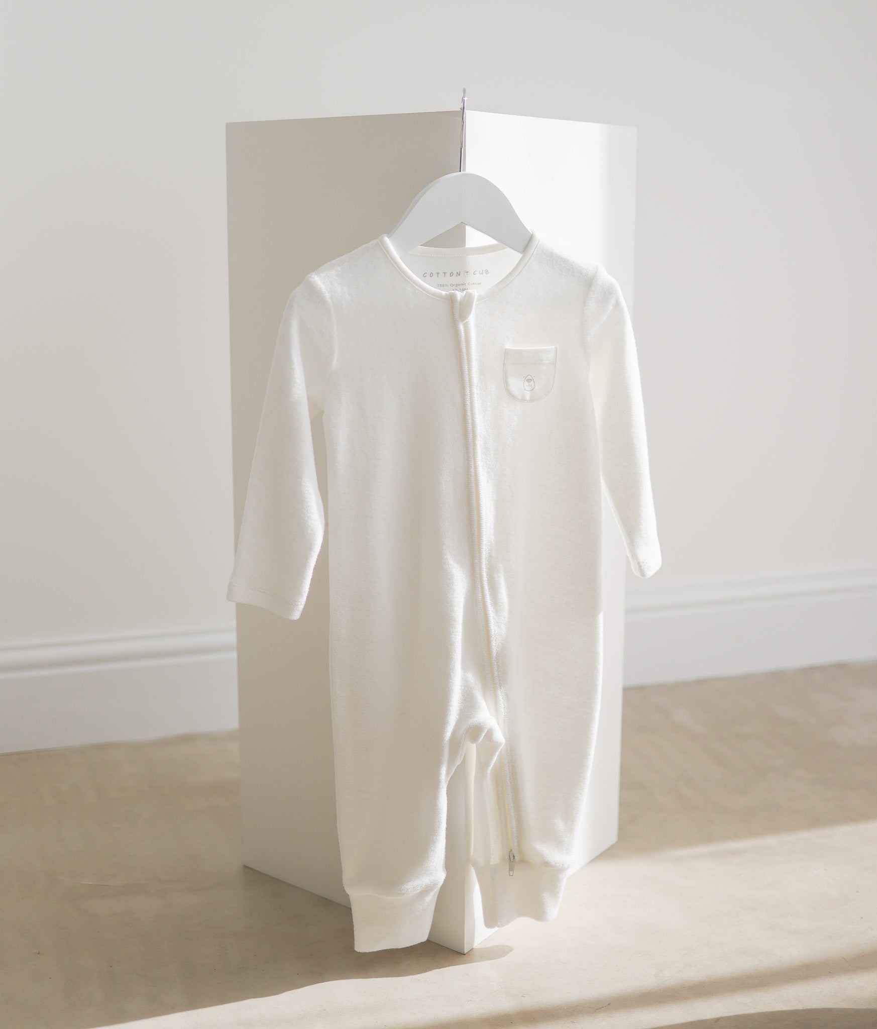 White baby onesie on a hanger against a white wall