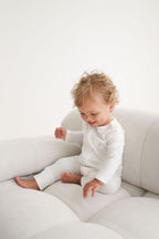 Child in a white outfit sitting on a light gray couch against a white background