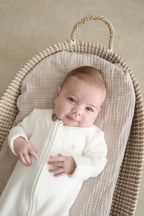 Baby in a white outfit lying in a woven basket with a neutral background