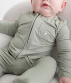 Baby wearing a green onesie with a logo on a light background