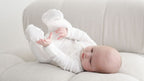 Baby in a white outfit lying on a light-colored couch