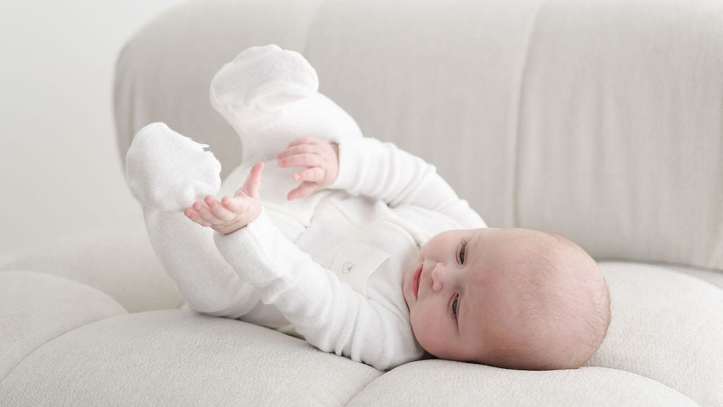 Baby in a white outfit lying on a light-colored couch