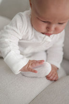Baby in a white outfit sitting on a light-colored surface