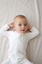 Baby wearing a white onesie against a plain background