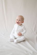 Baby in a white onesie sitting on a white blanket