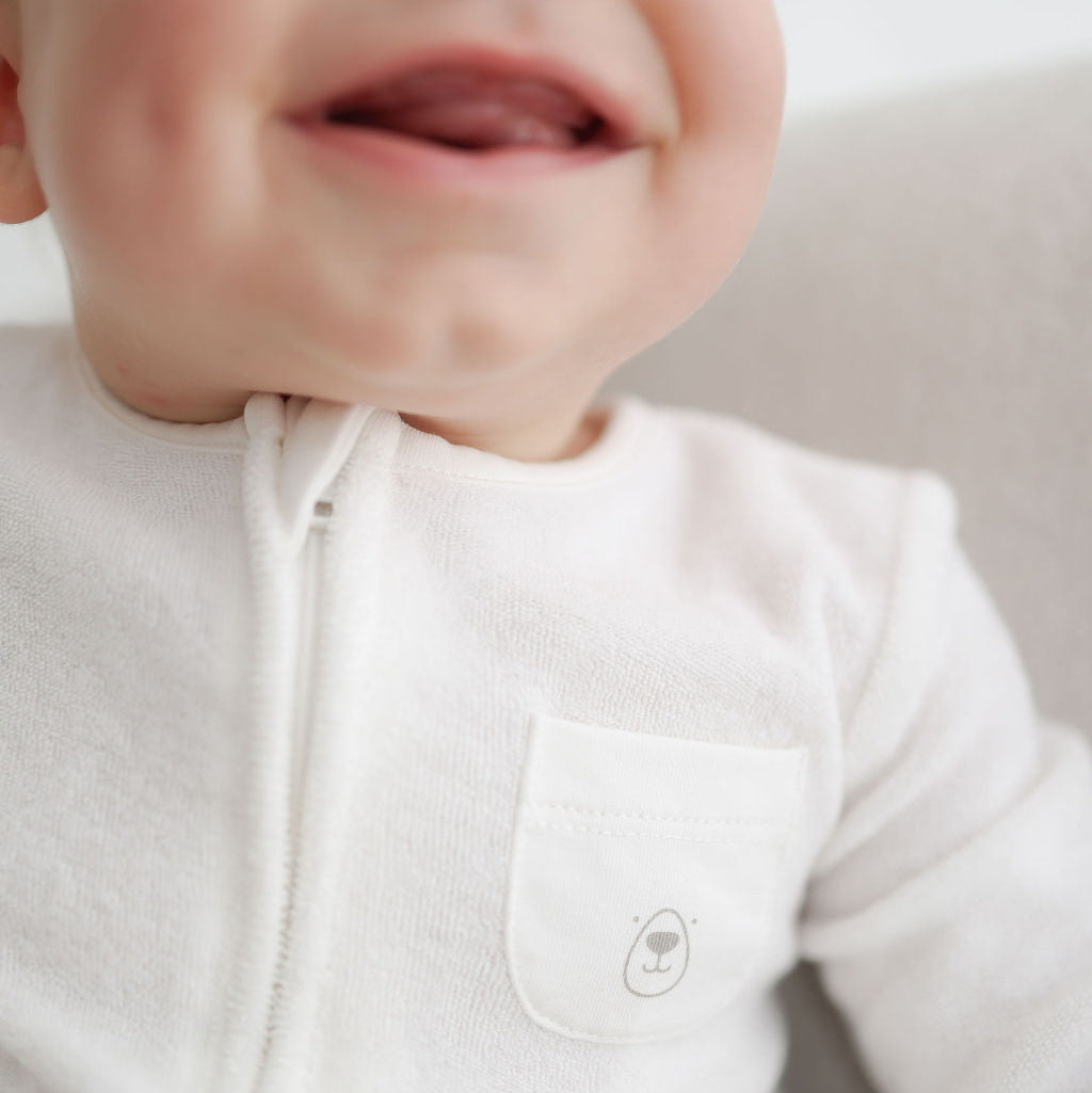 Close-up of a baby wearing a white onesie with a small logo on the chest.